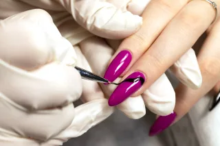 Magenta gel polish being applied to almond-shaped nails